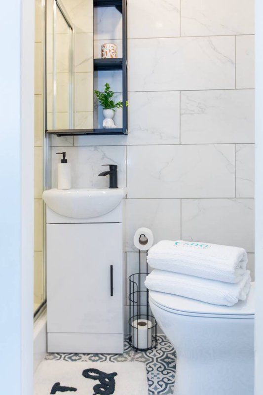 Modern bathroom with white sink, toilet, shelving, towels and patterned floor tiles