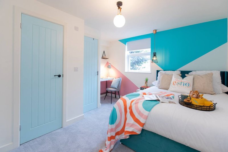 Bright bedroom with turquoise accent wall, double bed with colorful bedding, and light blue doors