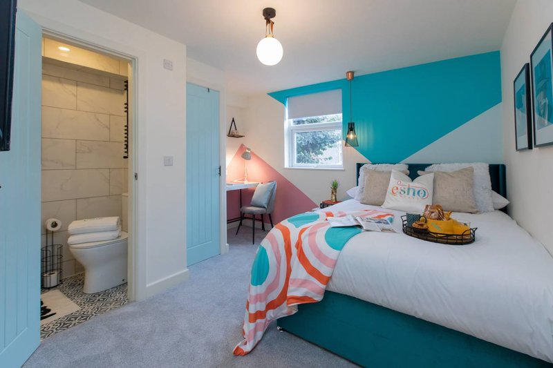 Bright bedroom with turquoise accent wall, double bed, ensuite bathroom, and colorful bedding