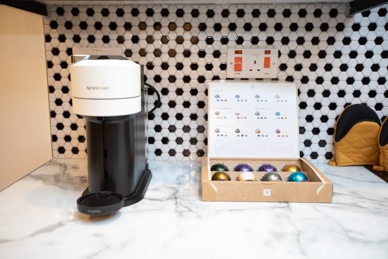 Kitchen counter with coffee maker, capsule organizer, and marble surface against patterned backsplash