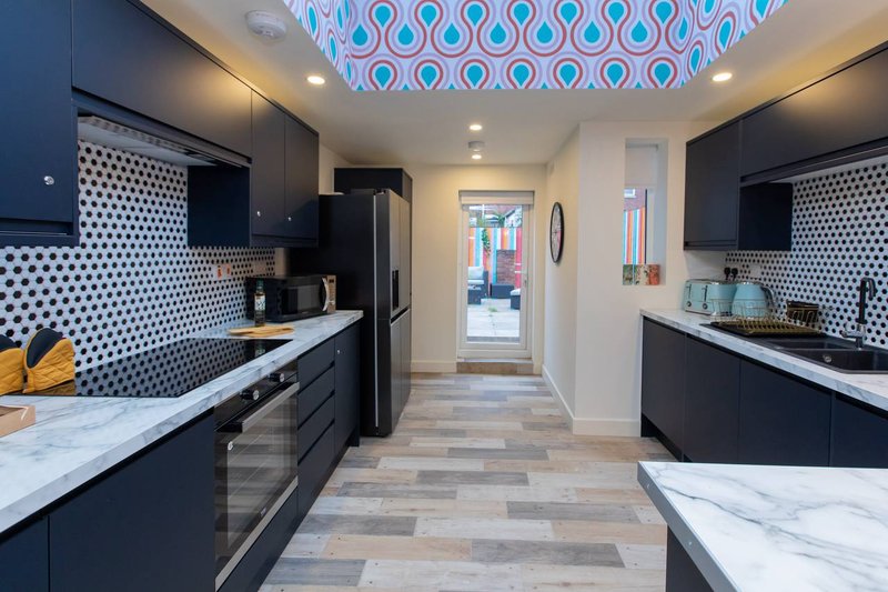 Modern kitchen with black cabinetry, white marble countertops, geometric tile backsplash and blue ceiling.