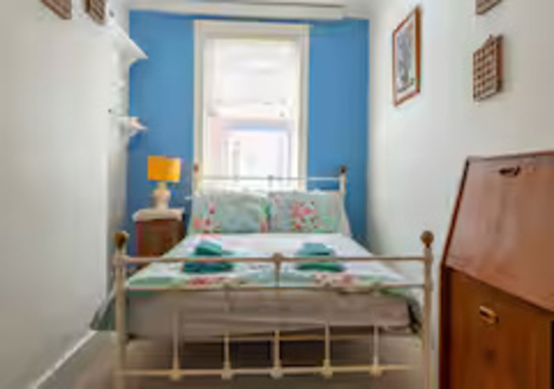 Bright bedroom with metal bed frame, blue accent wall, colorful bedding and window view