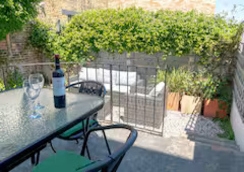 Outdoor patio area with dining table, wine bottle, chairs and ivy-covered walls
