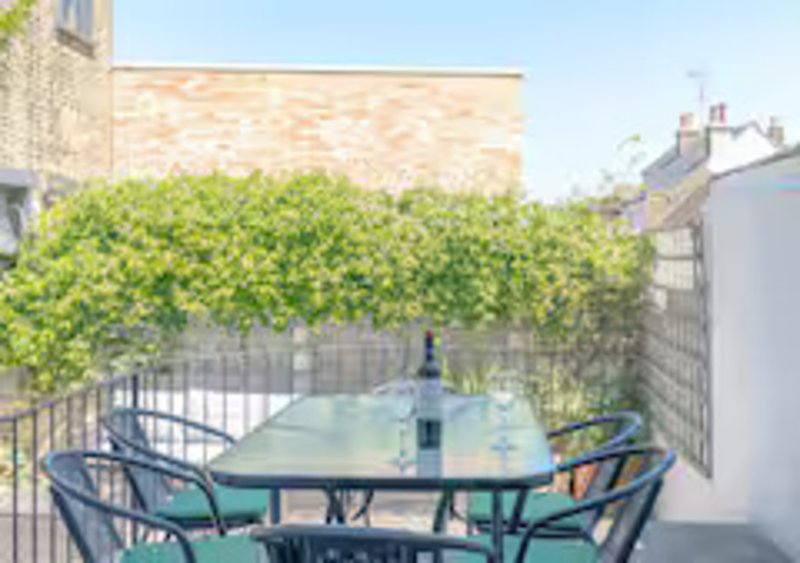 Outdoor terrace with table, chairs, ivy-covered fence and city buildings