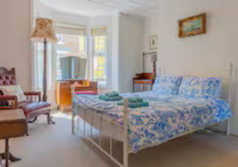 Bright bedroom with blue patterned bedding, white metal bed frame, pink chair and window