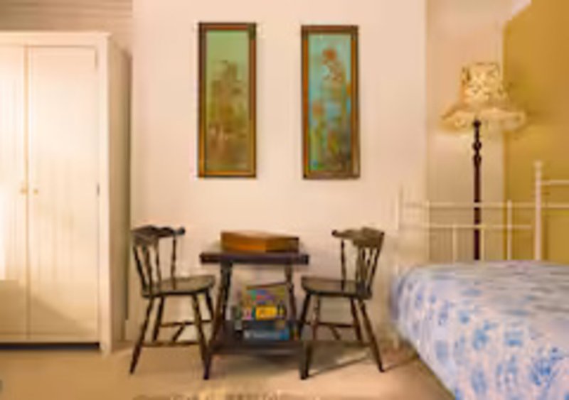 Bedroom with double bed, small dining table, two chairs, framed wall art and floor lamp