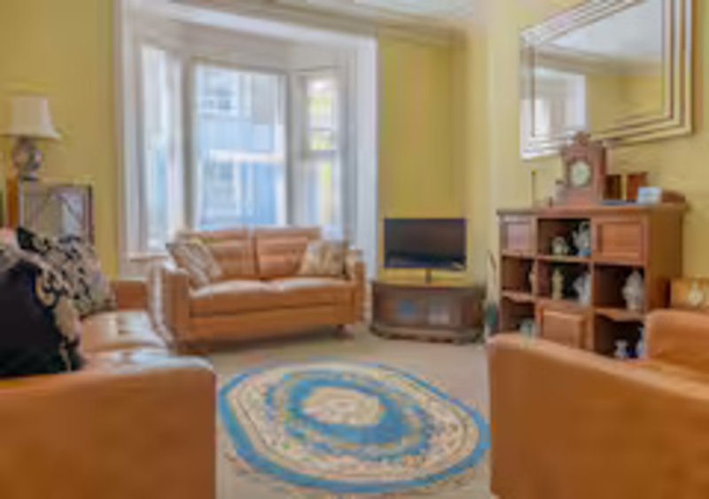 Bright yellow living room with tan leather sofas, blue circular rug, wooden shelving and TV