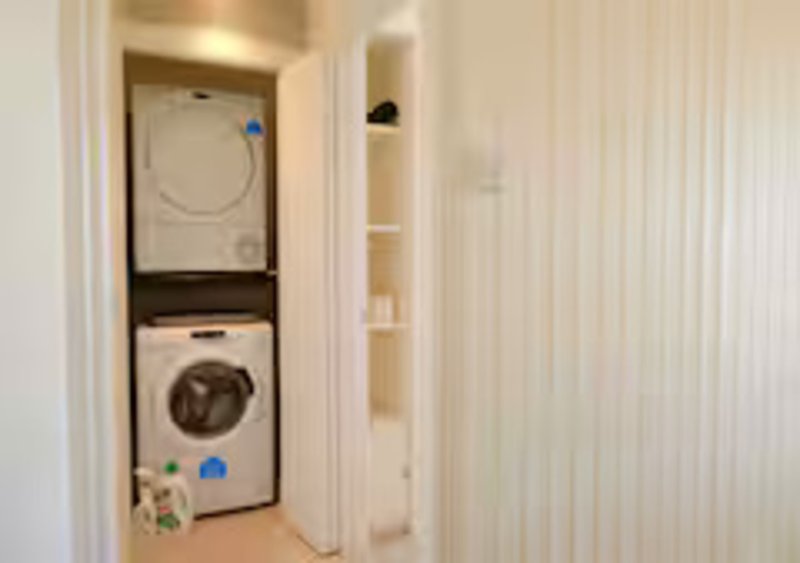 Laundry closet with stacked white washing machine and dryer, cream walls and shelving