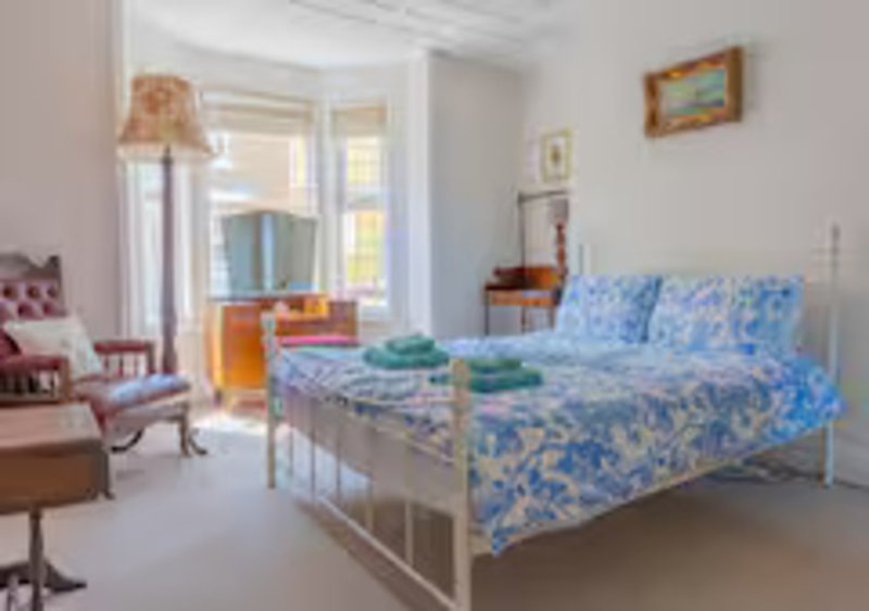 Bright bedroom with blue patterned bedding, metal bed frame, pink armchair and window doors