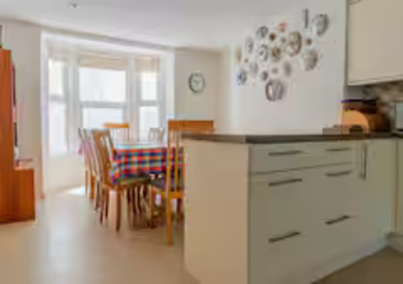Open-plan kitchen and dining area with sage green cabinetry, wooden table and chairs, decorative plates on wall