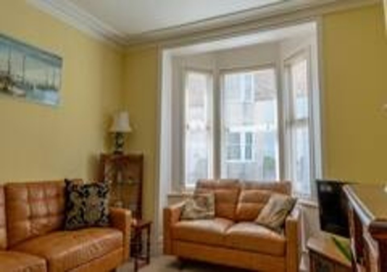 Bright yellow living room with tan leather sofa, armchair, and bay windows
