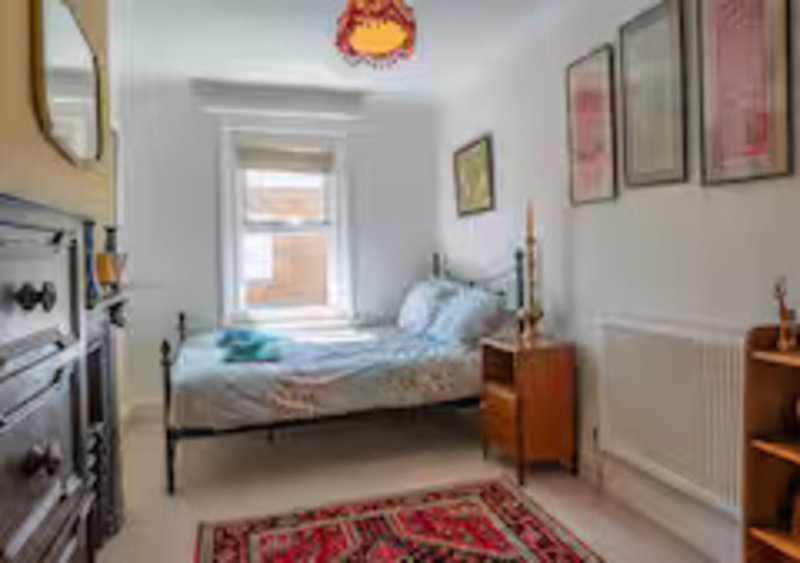 Bright bedroom with single bed, wooden bedside tables, framed wall art and window