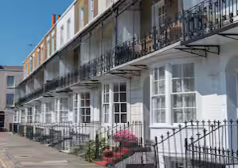 Georgian white townhouses with black railings, balconies and potted flowers lining a pedestrian street
