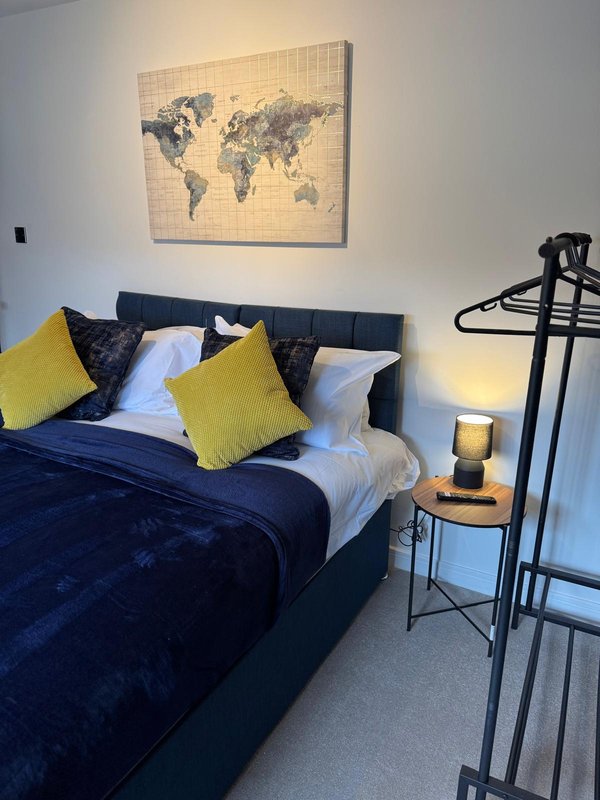Bedroom with dark blue bed, yellow cushions, world map wall art, and bedside lamp