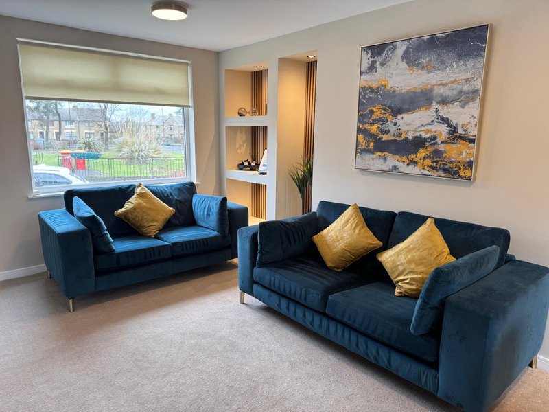 Modern living room with two blue velvet sofas, gold cushions, wall art, and large window with garden view