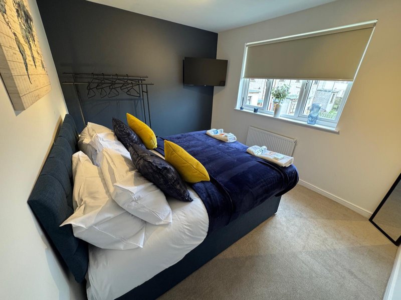 Modern bedroom with double bed, yellow and black cushions, white bedding and wall-mounted TV