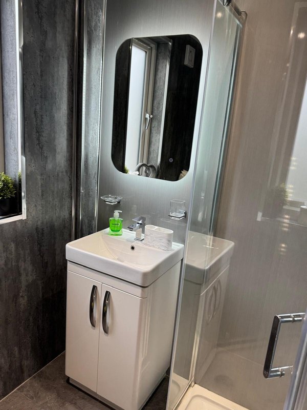 Modern bathroom with white vanity unit, illuminated mirror, and shower enclosure