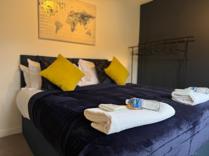 Bedroom with double bed, yellow cushions, white towels, and world map wall art
