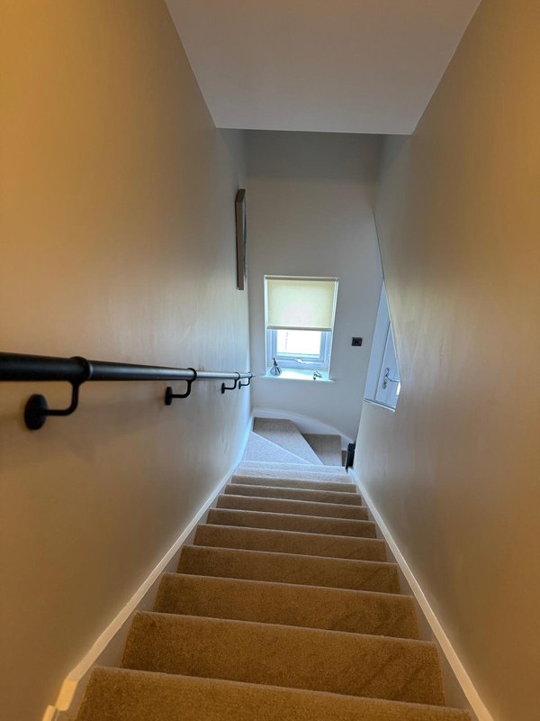 Staircase with brown carpet, cream walls, black handrail, and window at top
