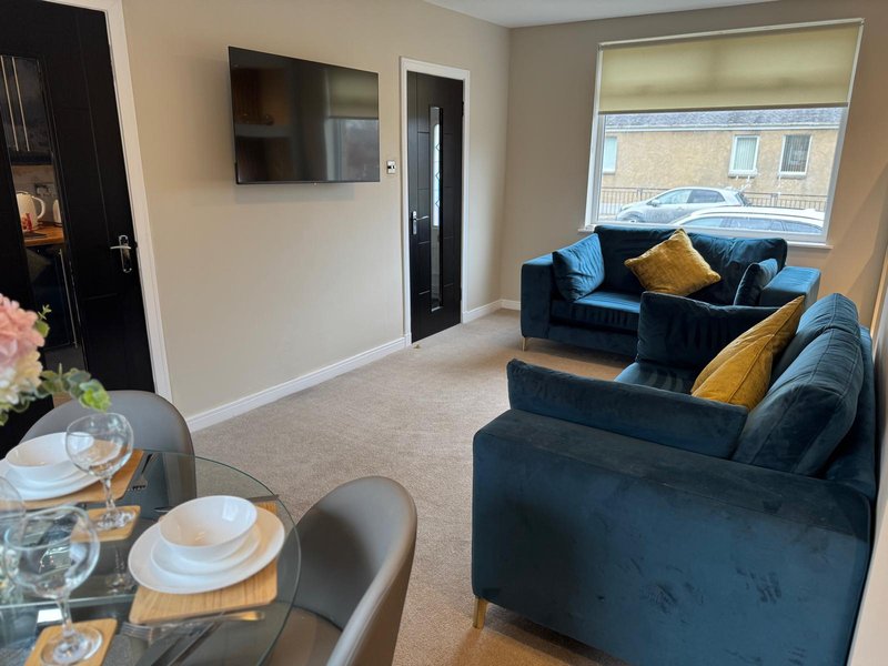 Open-plan living room with dining table, blue velvet sofas, wall-mounted TV and large window