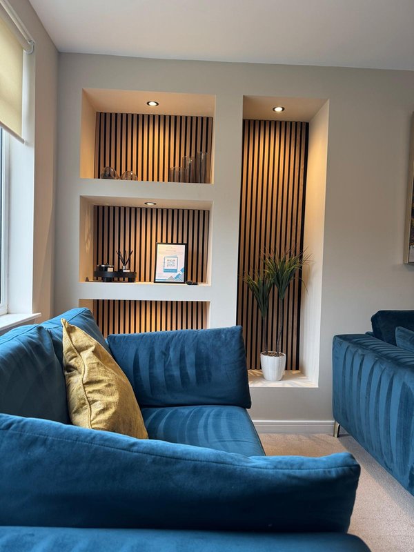 Modern living room with blue sectional sofa, built-in wooden shelving, and natural lighting from window