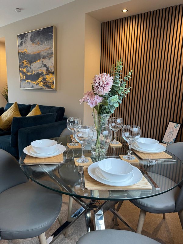 Dining table set for two with flowers, glasses, and place settings in modern living room