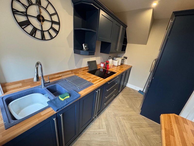 Modern kitchen with dark cabinetry, wooden countertops, sink, and wall-mounted clock