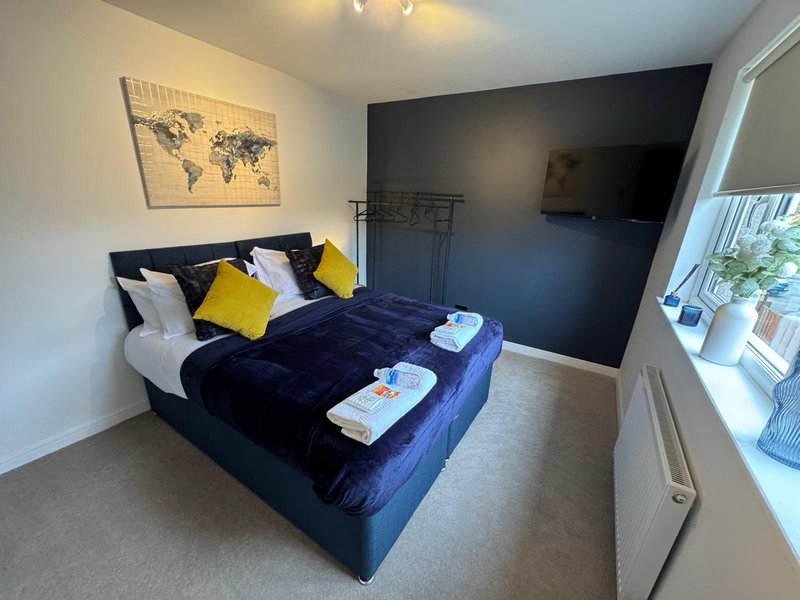 Bedroom with double bed, navy bedding, yellow cushions, world map artwork, and feature wall