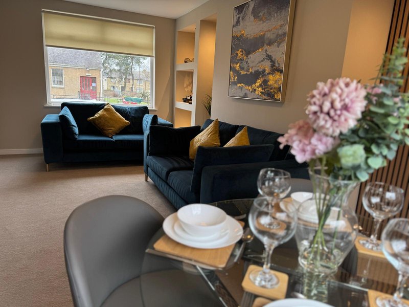 Modern living room with navy velvet sofas, dining table with place settings and flowers in foreground
