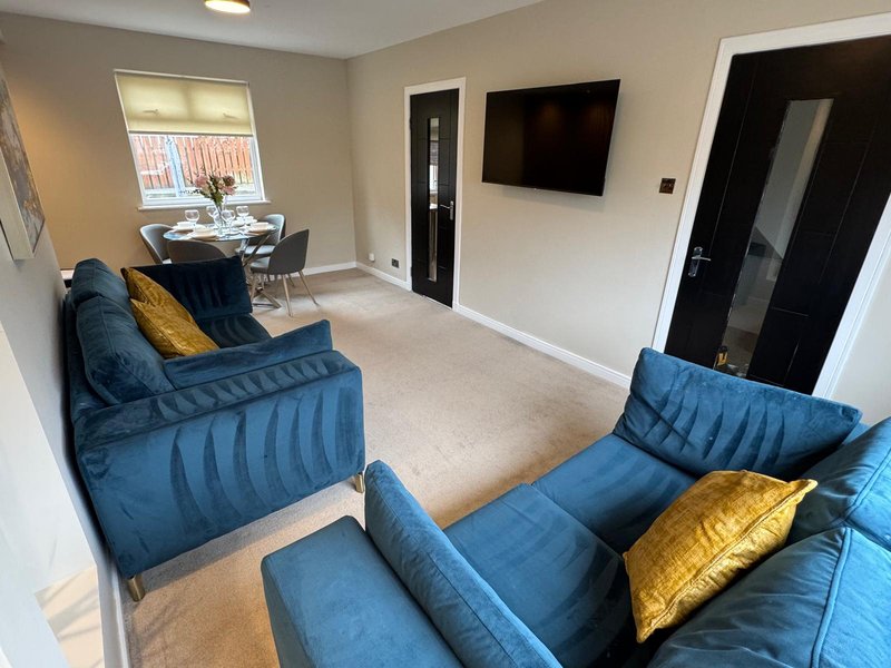 Modern living room with blue upholstered seating, gold cushions, TV, and dining area visible