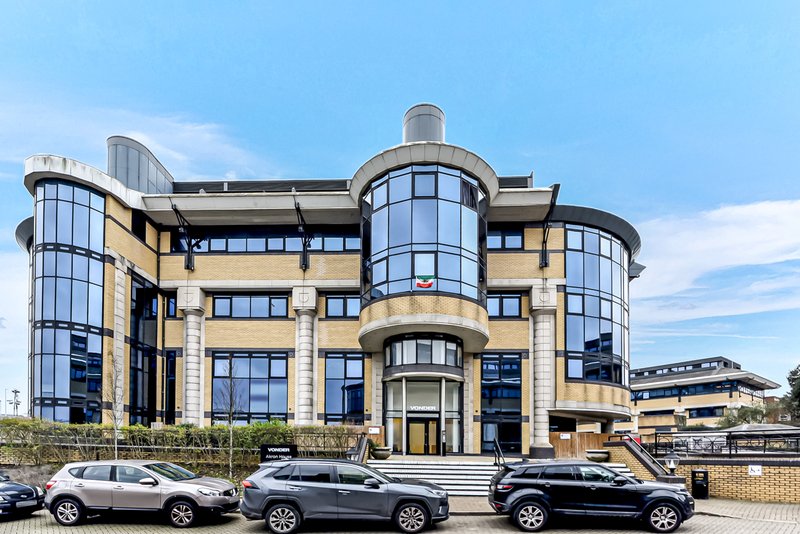 Modern curved stone building with large windows, parked cars in front, clear sky