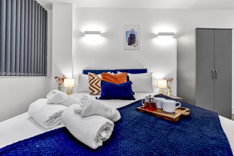 Modern bedroom with blue bed, white pillows, rolled towels, and contemporary wall lighting