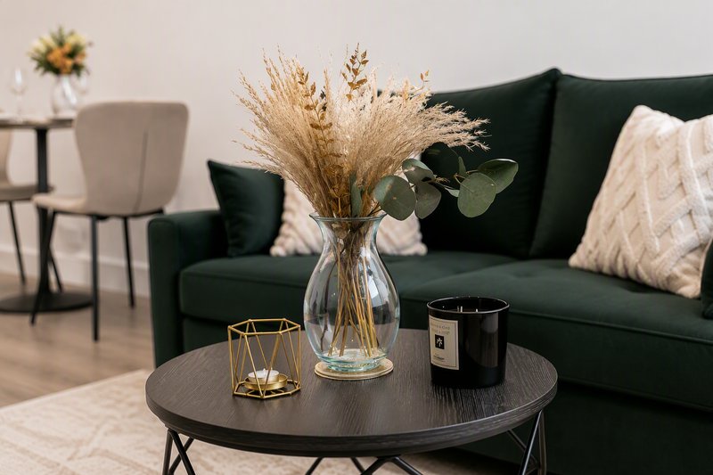 Modern living room with dark green sofa, round black coffee table, dried flower arrangement and decorative candle