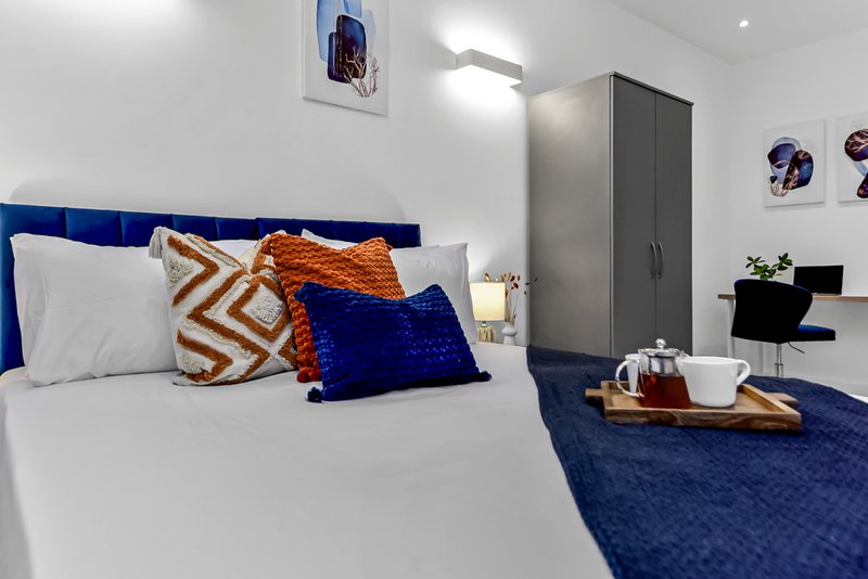 Modern bedroom with blue headboard, white bedding, patterned cushions and wardrobe