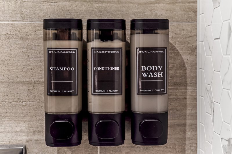 Three wall-mounted bathroom dispensers containing shampoo, conditioner, and body wash