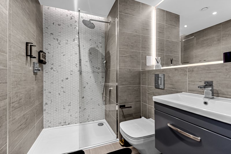 Modern bathroom with walk-in shower, dark vanity, white sink and mirror lighting