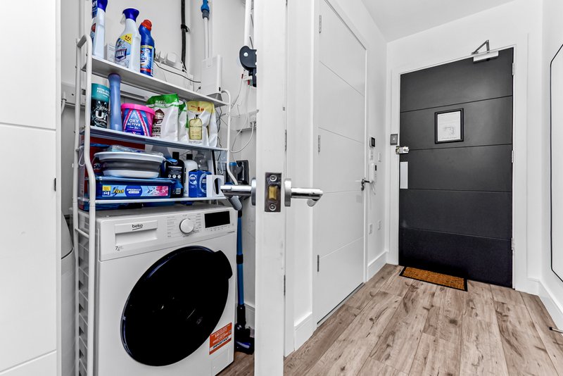 Utility room with white washing machine, shelving with cleaning supplies, and black entry door