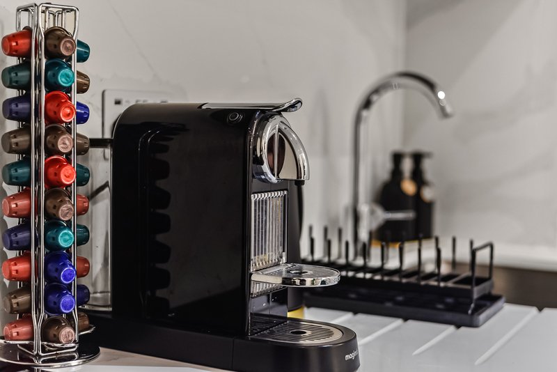 Kitchen countertop with black coffee machine, colorful capsule storage tower, and drying rack