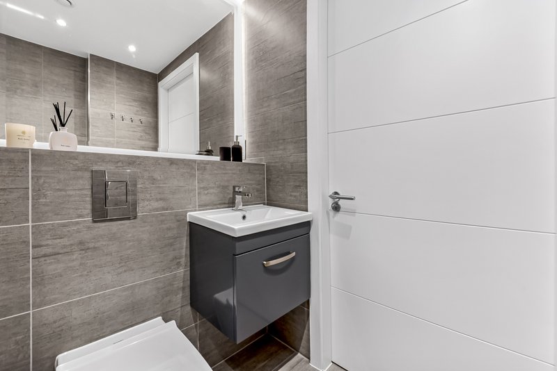 Modern bathroom with gray tile walls, white sink, black vanity unit and large mirror