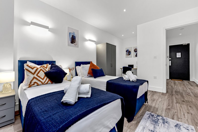 Modern bedroom with two twin beds, blue bedding, white walls and recessed lighting
