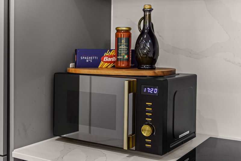 Modern microwave with shelf above displaying bottles and packaged food items