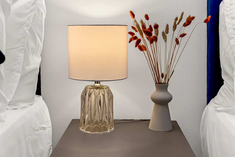 Bedside table with decorative lamp, dried flower arrangement, and white pillows on either side