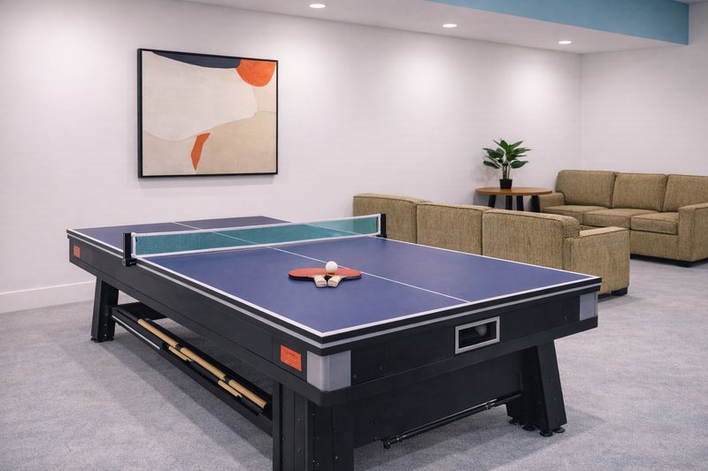 Games room with blue ping pong table, tan upholstered seating, abstract wall art, and potted plant