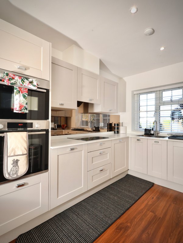 Modern white kitchen with built-in appliances, island counter, and window overlooking garden