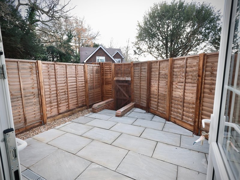 Paved garden patio area enclosed by wooden fence panels with house visible beyond