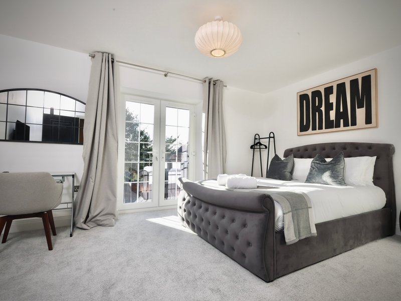 Modern bedroom with grey upholstered bed, white bedding, pendant light and patio doors