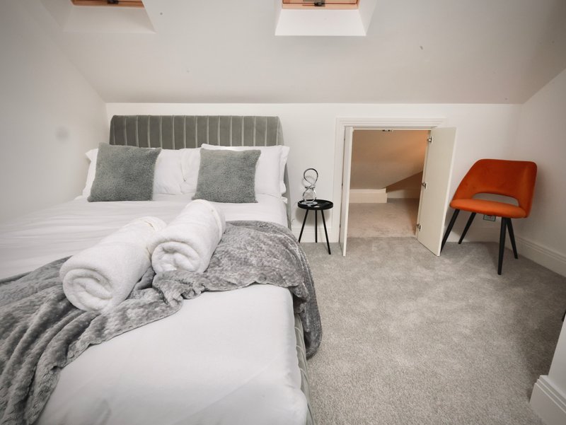 Modern bedroom with double bed, gray headboard, rolled towels, and orange accent chair