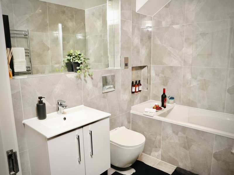 Modern bathroom with white vanity, toilet, bathtub, large mirror and beige tile walls