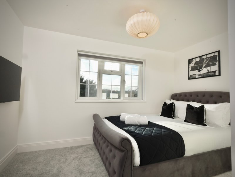 Modern bedroom with double bed, dark headboard, black quilted throw, white pillows, and window with grey frame