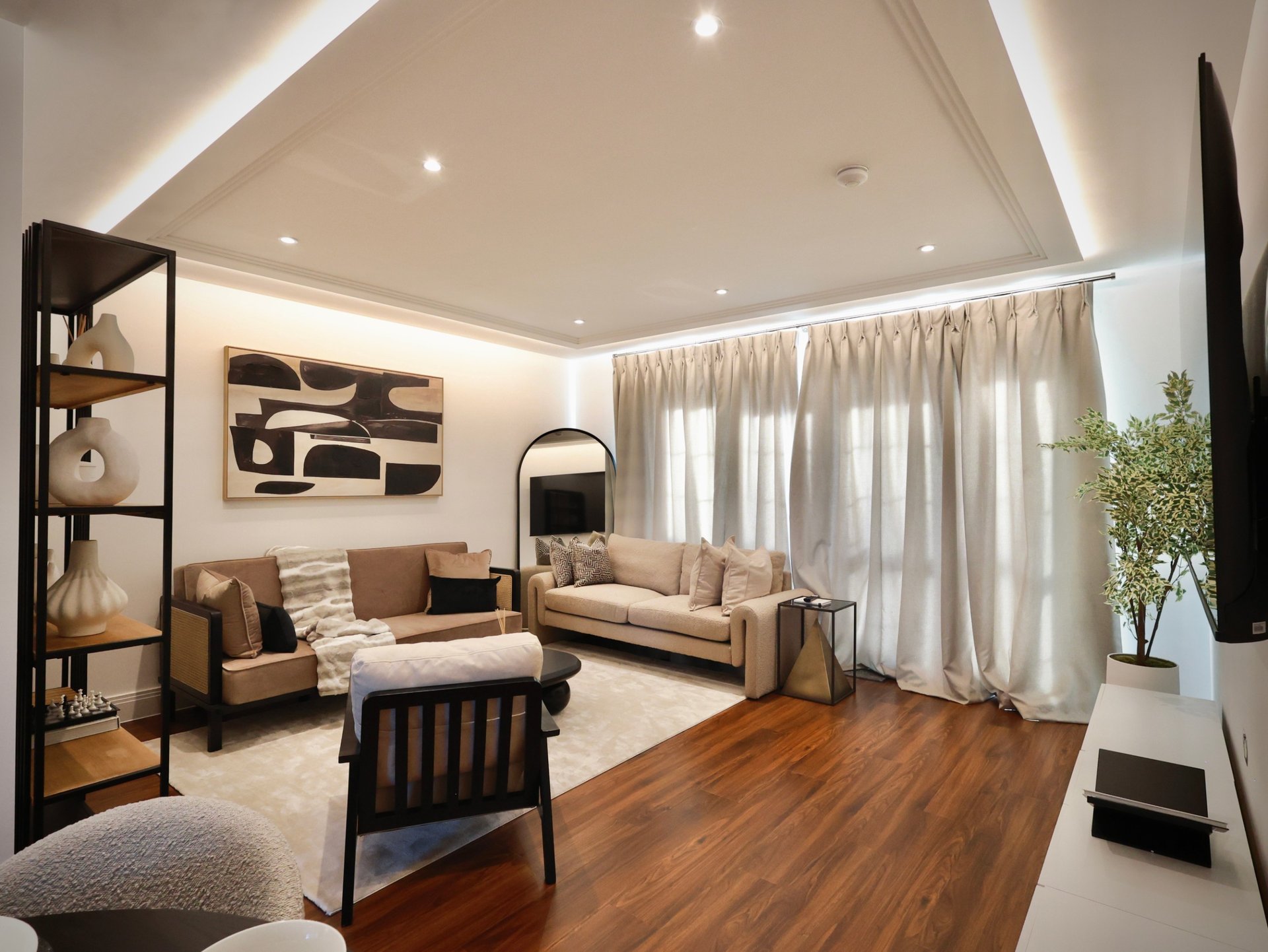 Modern living room with beige sofa, armchair, wooden floor, and floor-to-ceiling curtains